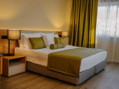 Modernes Hotelzimmer mit Doppelbett, grünen Vorhängen und warmen Lichtakzenten.