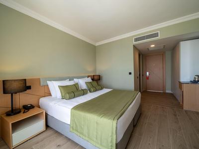 Modernes Hotelzimmer mit großem Bett, grüner Bettdecke, Nachttischlampen und Holzmöbeln.
