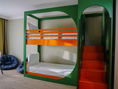 Grünes Etagenbett mit orangefarbenen Treppen und weißer Matratze in hellem Raum.