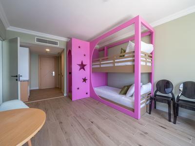 Modernes Hotelzimmer mit Etagenbett in Pink, zwei schwarzen Stühlen und Holzfußboden.