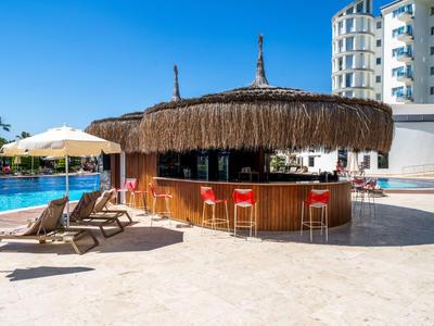 Moderner Poolbar mit Strohdach und roten Barhockern neben Liegestühlen an einem Hotelpool.