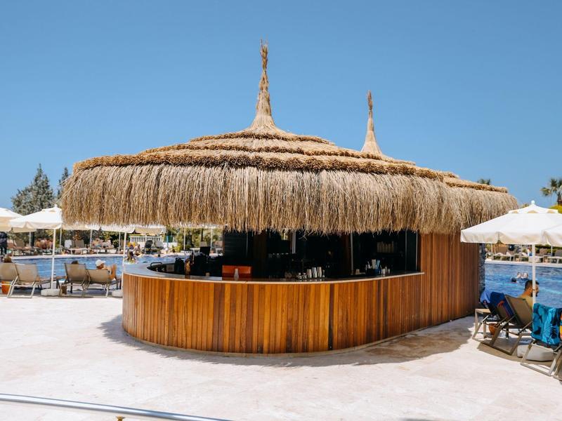 Okrągły bar z drewna z dachem ze słomy pod jasnym niebem przy basenie.