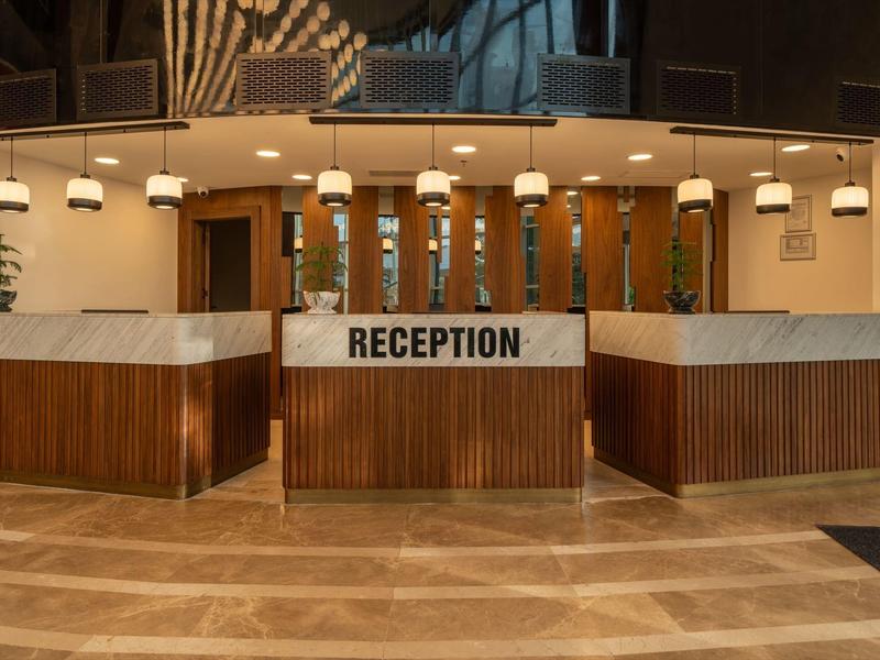 Nowoczesny drewniany recepcjon z wiszącymi lampami i marmurowymi panelami.