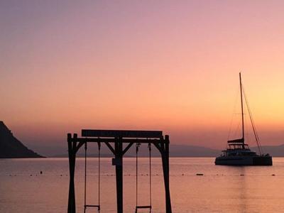 Západ slunce nad klidným mořem s houpačkou a plachetnicí ve vodě.