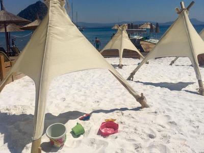 Several tipis stand on the beach with white sand under a clear blue sky.