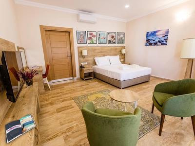 Moderně zařízený hotelový pokoj s manželskou postelí, dvěma zelenými křesly a dřevěnou podlahou.