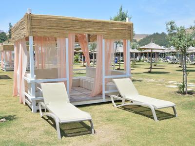 Pavilon s bílými závěsy a dvěma lehátky na zelené trávě za slunečného počasí.