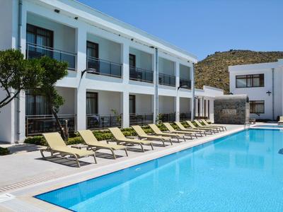 Modern hotel pool with sun loungers in front of a white building under blue sky.