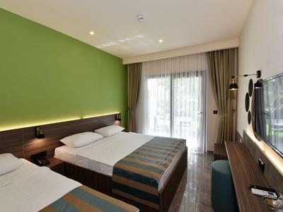 Nowoczesny pokój hotelowy z dwoma łóżkami, zieloną ścianą i balkonem z zasłonami.