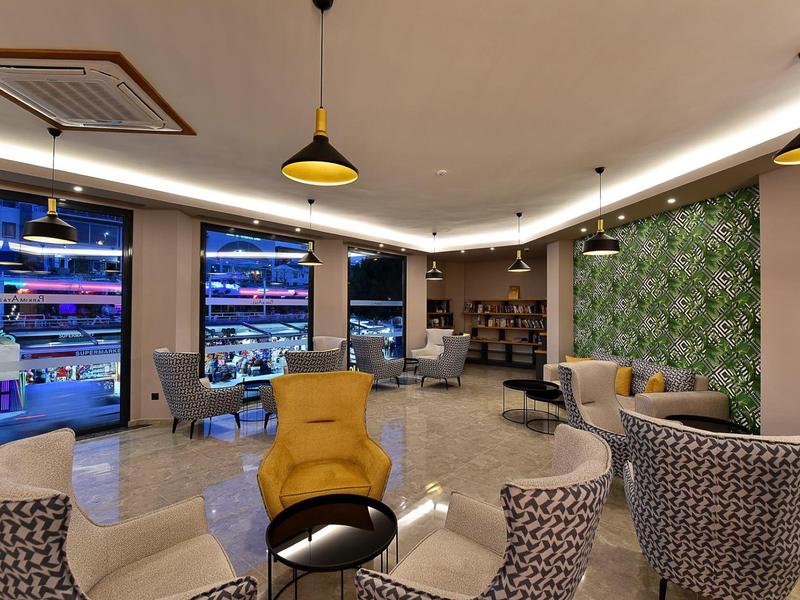 Spacious hotel lounge with modern chairs, yellow armchairs, a green wall, and large windows.