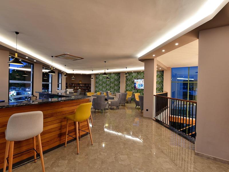 Modern hotel lounge with wooden bar, colorful chairs, and polished marble floor.