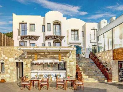 Hotel bianco moderno con bar all'aperto e aree salotto sotto un cielo blu.