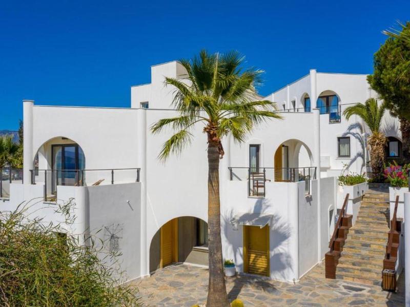 Edificio bianco con archi, palme e terrazza sotto un cielo azzurro limpido.