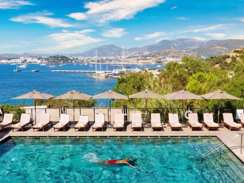 Piscina con lettini e ombrelloni, vista sul mare e yacht sotto un cielo sereno.