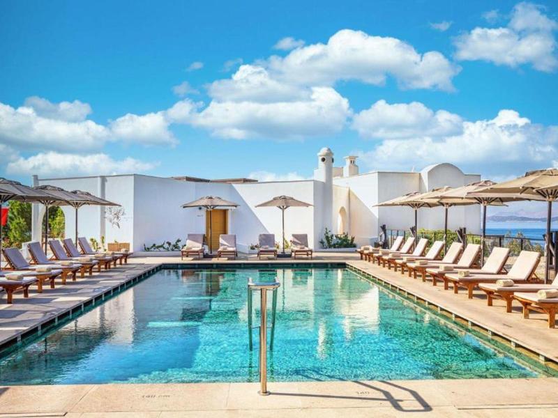 Area piscina lussuosa con lettini e ombrelloni sotto un cielo azzurro.