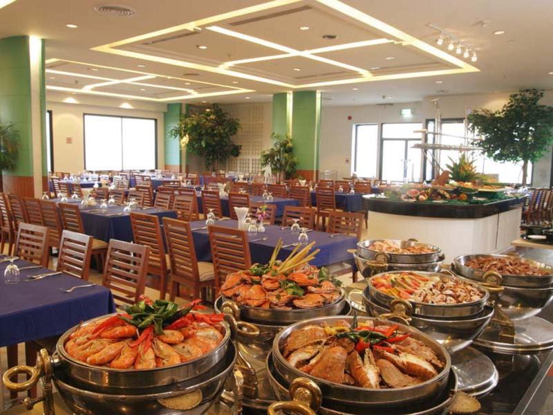 Großer Speisesaal mit dekoriertem Buffet und gedeckten Tischen, Holzstühlen und Pflanzen.