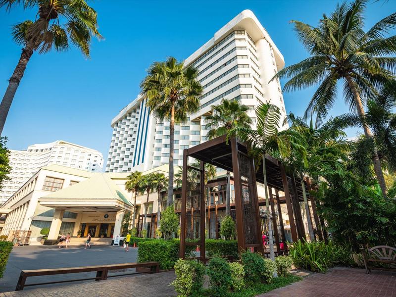 Hotelgebäude mit weißen Fassaden, umgeben von hohen Palmen und einem ruhigen Gartenbereich.