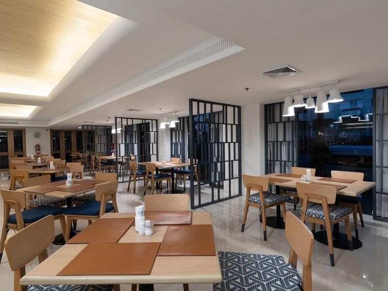 Moderner, heller Gastraum mit Holzstühlen, Tischen und großen Fenstern in klarem Design.