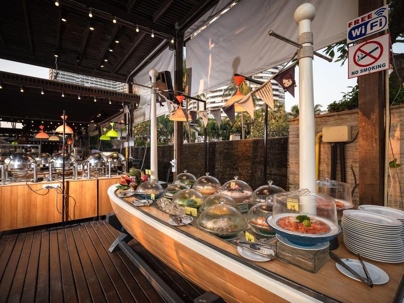 Buffet auf hölzernem Boot mit verschiedenen Salaten und Speisen in einem Gartenrestaurant.