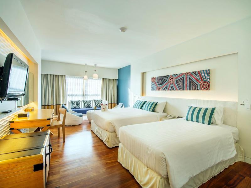 Hell eingerichtetes Hotelzimmer mit zwei großen Betten, Holzfußboden und modernem Dekor.