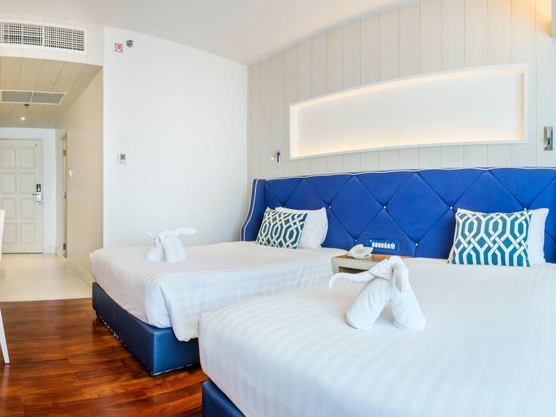 Modernes Hotelzimmer mit zwei weißen Einzelbetten, blauem Kopfteil und Holzboden.