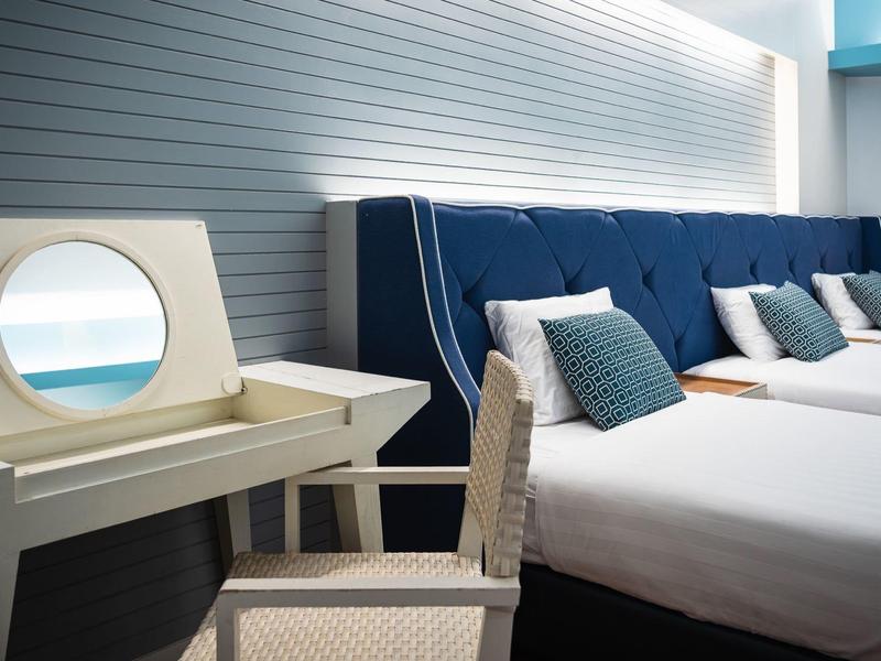 Modernes Schlafzimmer mit blauem Polsterbett, weißen Betten, grauer Wand und einem Schminktisch mit rundem Spiegel.