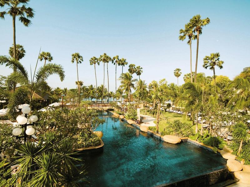 Grüner Park mit hohem Palmen, Teich in der Mitte und hellblauem Himmel im Hintergrund.