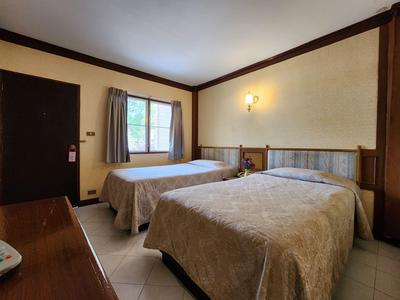 Einfaches Hotelzimmer mit zwei Einzelbetten, Fenster, Vorhängen und dunkler Tür.