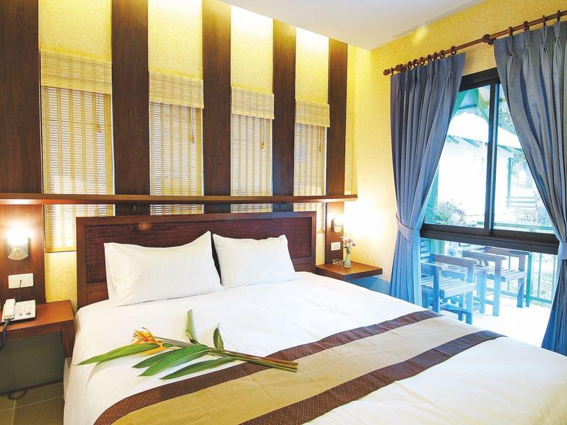 Modern hotel room with large bed, decorative flower, and balcony view with blue curtains
