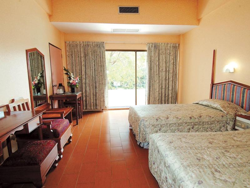 Twin bedroom with wooden furniture, desk, and terrace overlooking greenery.