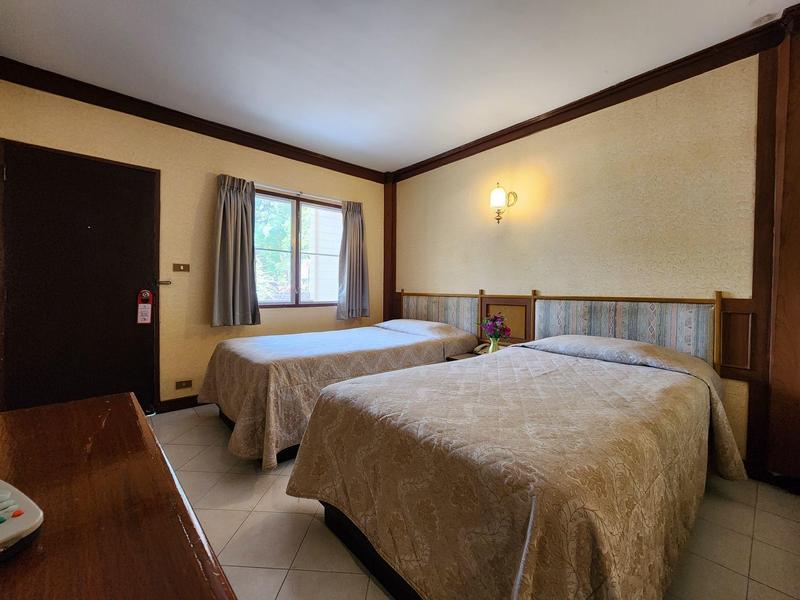 Hotel room with two single beds, window with curtains, and simple furnishings.