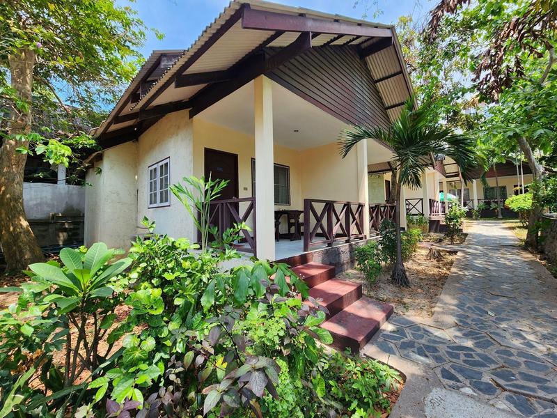 Small vacation cottage with porch in a tropical garden next to a paved path.