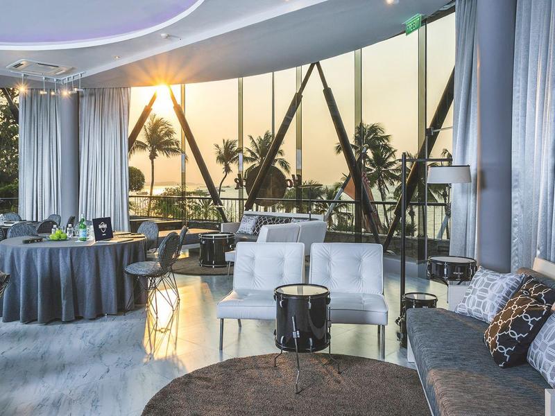 Moderne Lounge mit großen Glasfenstern, weißen Sesseln, runden Tischen und Tageslicht.