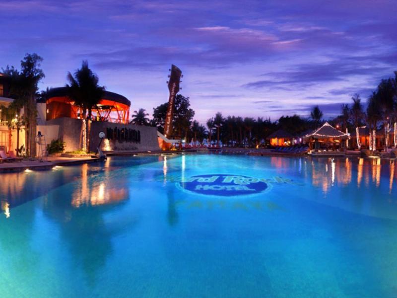 Großer beleuchteter Pool bei Sonnenuntergang mit umliegenden Gebäuden und reflektierendem Wasser.