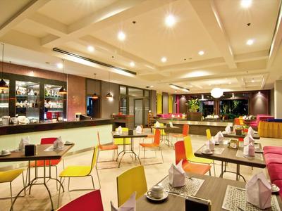 Helles Café mit bunten Stühlen, runden Tischen und modernem Deckenlicht.