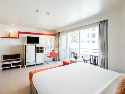 Modernes Schlafzimmer mit großem Bett, TV, Schreibtisch und bodentiefen Fenstern, viel Tageslicht.