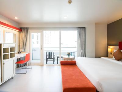 Helles Schlafzimmer mit großem Bett, orangerotem Sitzbank, Schreibtisch und Balkon mit Stühlen.