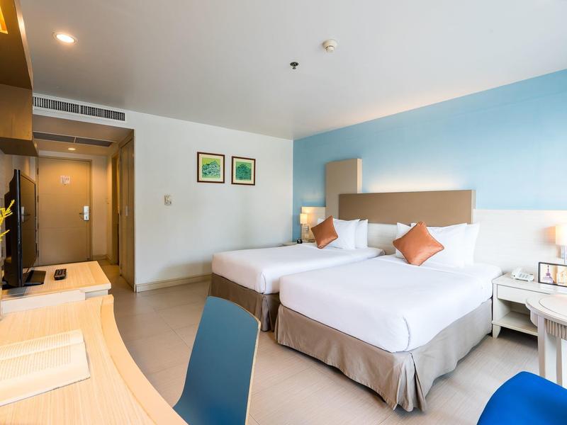 Modernes Hotelzimmer mit zwei Betten, blauer Wand, Schreibtisch und Stuhl, hell und sauber gestaltet.