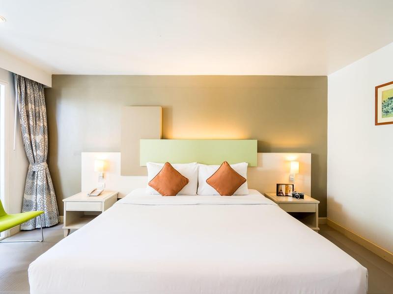 Helles Hotelzimmer mit großem Doppelbett, grüner Wand, zwei Nachttischen und grünem Sessel.