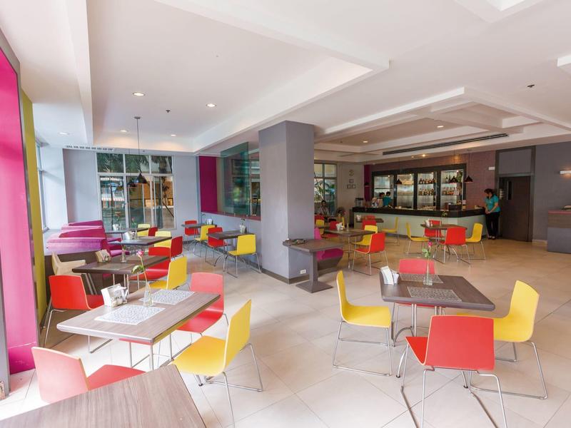 Heller Cafébereich mit bunten Stühlen, Tischen und großen Fenstern für viel Tageslicht.