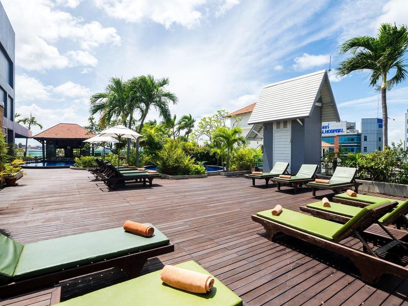 Terrasse mit Holzdeck, Liegestühlen und Palmen unter blauem Himmel mit Wolken.