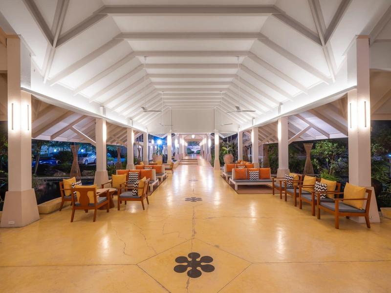 Weitläufige, helle offene Halle mit weißer Decke, Säulen und Holzmöbeln in warmen Tönen.