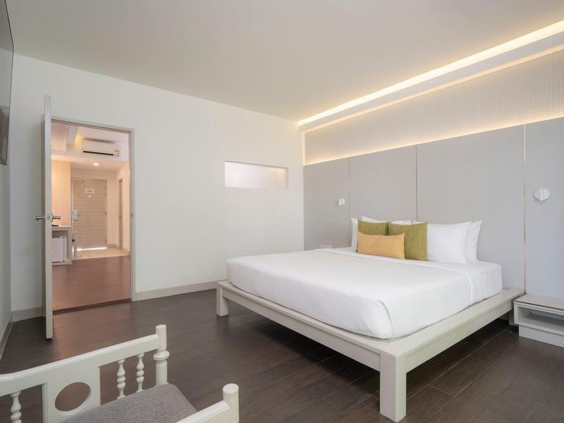 Modernes Schlafzimmer mit großem Bett, weißer Wand, indirekter Beleuchtung und offenem Badbereich.