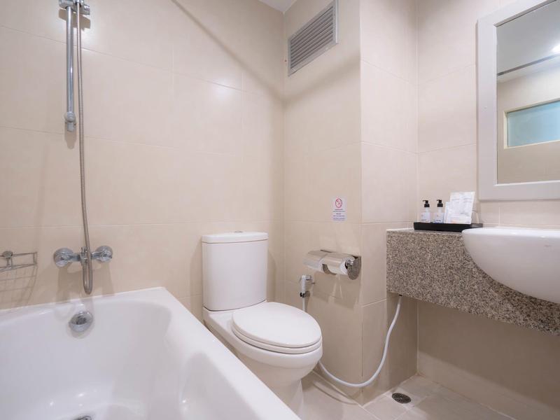 Kleines Badezimmer mit Badewanne, weißer Toilette, Waschbecken und Spiegel in neutralen Farbtönen.