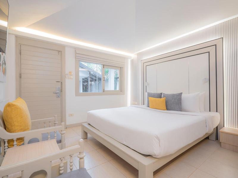 Helles, modernes Schlafzimmer mit weißem Bett, gelben Kissen und indirekter Lichtbeleuchtung.