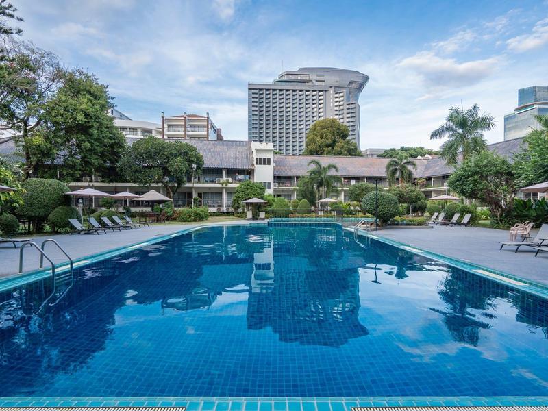 Großer blauer Pool mit klarer Wasseroberfläche, umgeben von Palmen und urbanen Hochhäusern.