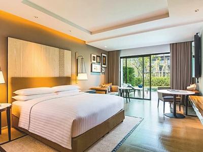 Habitación de hotel moderna con cama doble, escritorio, área de descanso y vista a una terraza con jardín.