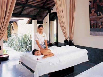 Woman receiving a massage in a bright, cozy spa room with curtains and plants.
