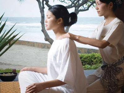 A woman receives a massage at a beachside spa area with sea view and trees in the background.