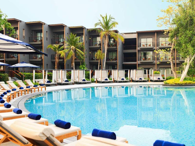 Large hotel pool with sun loungers and palm trees in a modern resort.